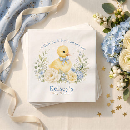 Dusty blue baby shower napkin with a yellow duckling wearing a blue bow, hydrangea and a personalized name in soft blue