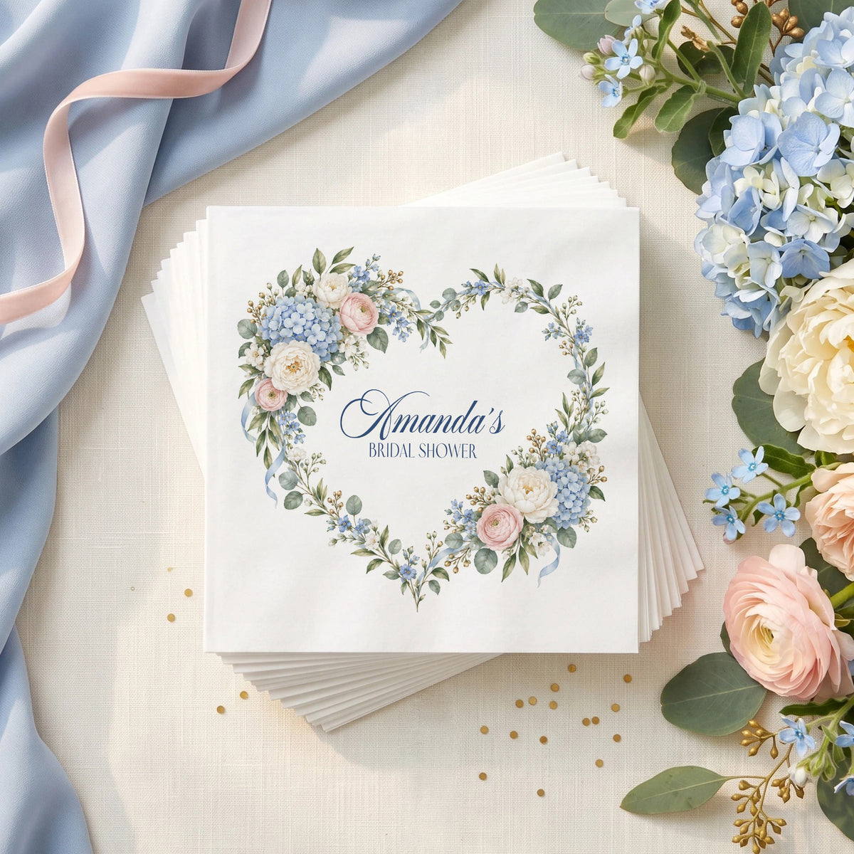 Personalized bridal shower napkin with a heart wreath of blue hydrangeas, blush roses, ivory flowers, ribbons and editable text