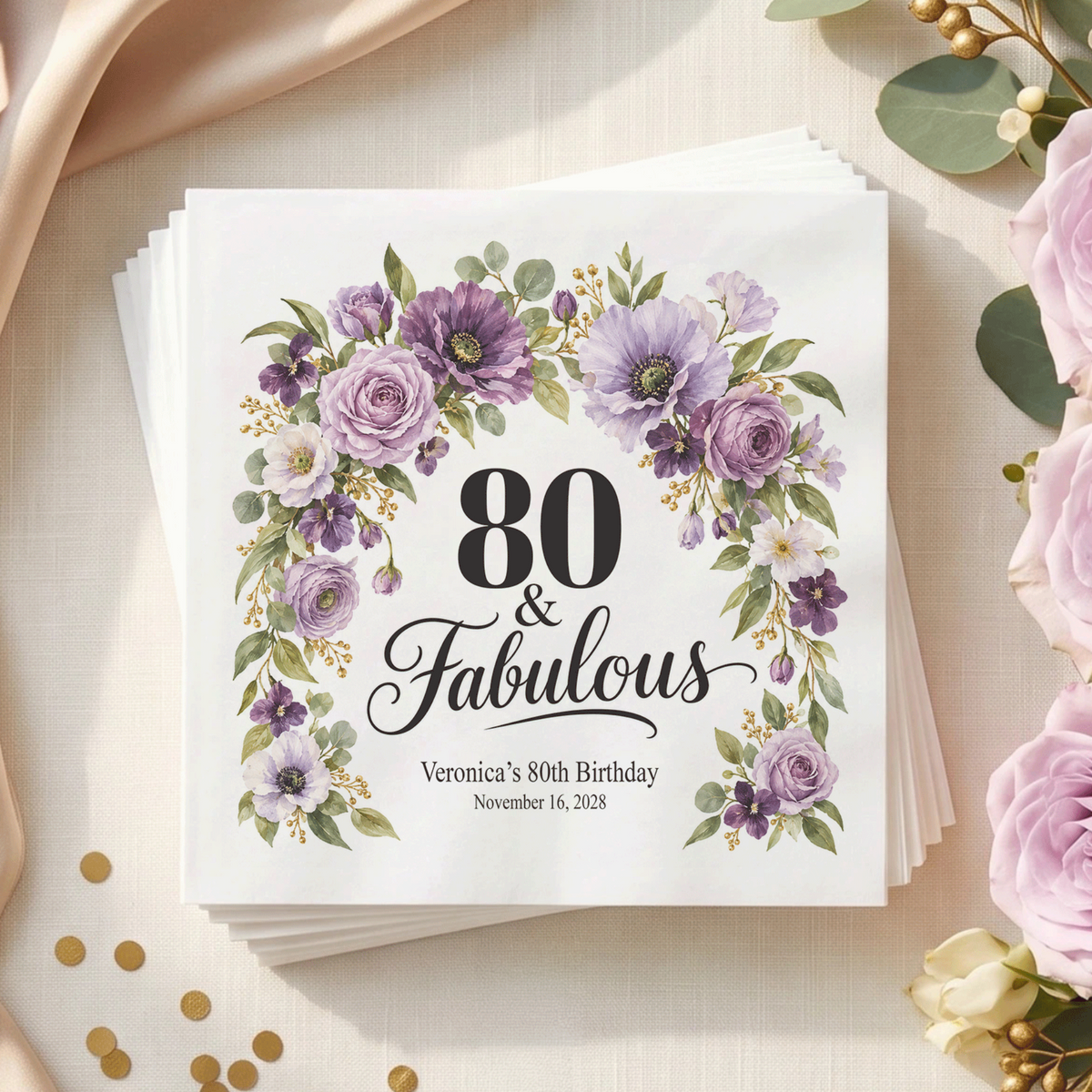 White napkin with “80 & Fabulous” in black, framed by a purple floral arch, with two personalized text lines below.
