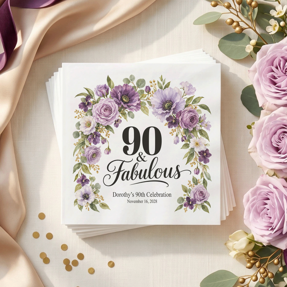 White napkin with “90 & Fabulous” in black, framed by a purple floral arch, with two personalized text lines below.