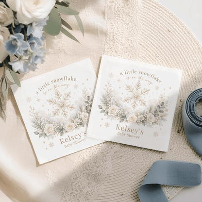 Two white baby shower napkins with snowflake and floral design, reading "Kelsey's Baby Shower".