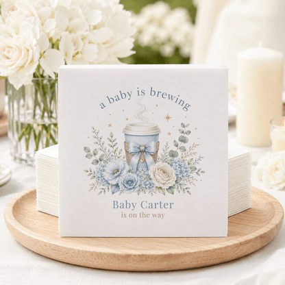 Napkins with blue floral design and text "a baby is brewing Baby Carter is on the way."