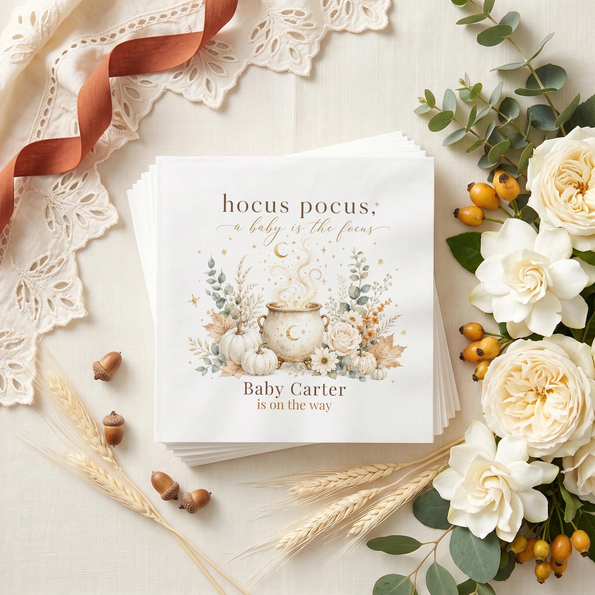 Cream and gold baby shower napkin with a moon marked cauldron, white pumpkins, ivory roses and a personalized baby name