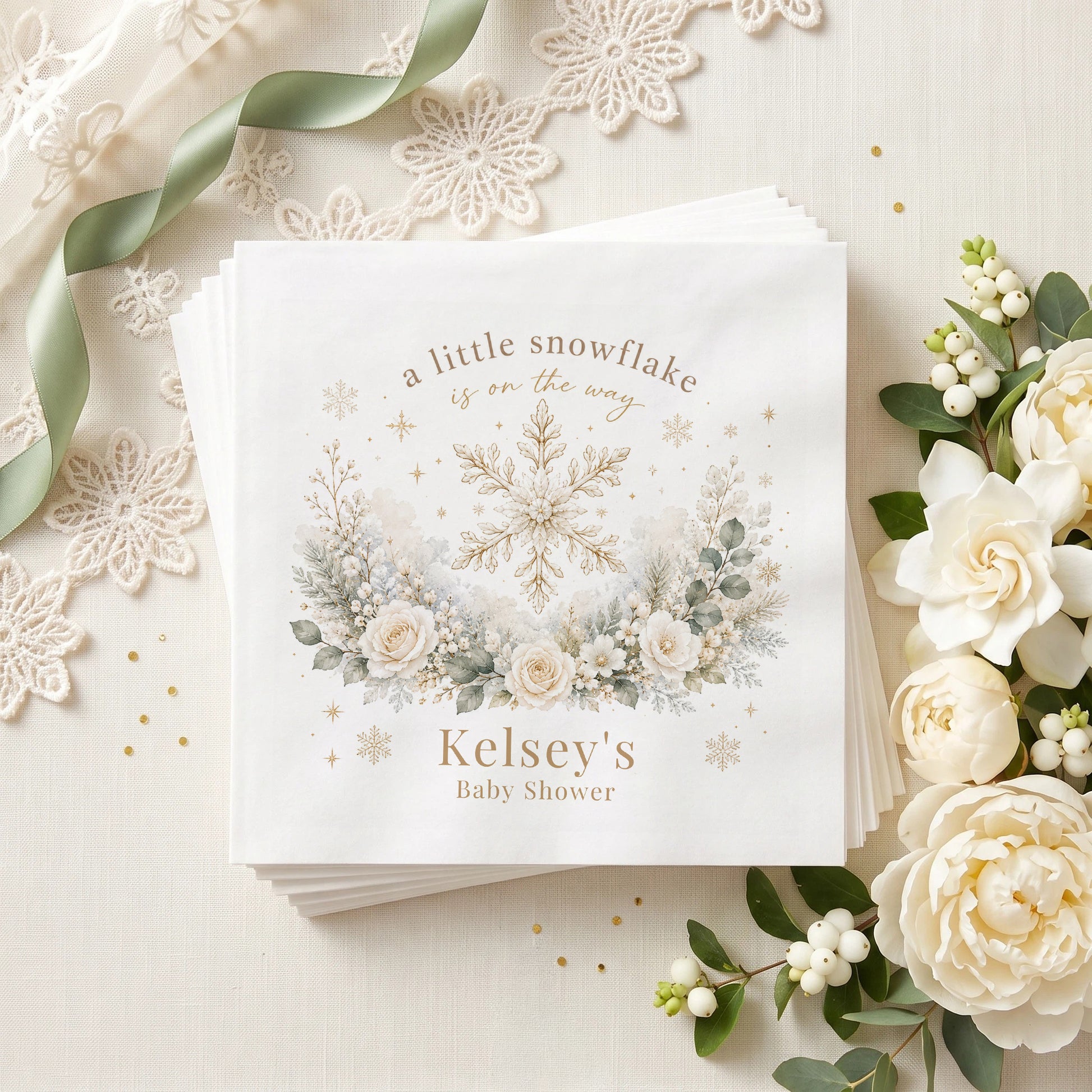 Ivory and gold baby shower napkin with a snowflake, cream roses, frosted greenery and a personalized name in warm taupe