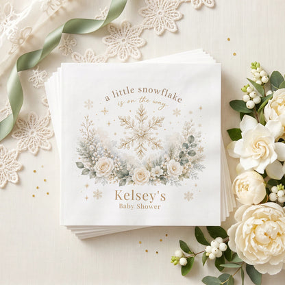 Ivory and gold baby shower napkin with a snowflake, cream roses, frosted greenery and a personalized name in warm taupe
