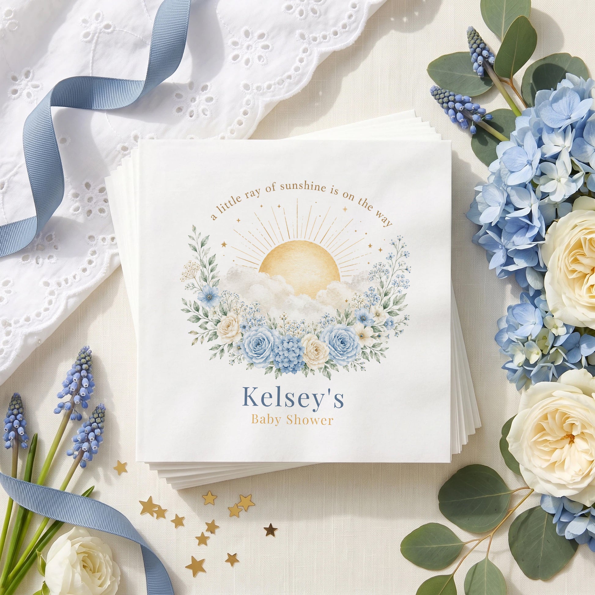 Dusty blue baby shower napkin with a gold rayed sun, white clouds, blue roses and a personalized name in deep blue