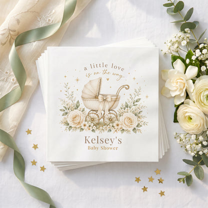 Cream and gold baby shower napkin with a vintage carriage, ivory bow, ivory roses and a personalized name in warm taupe