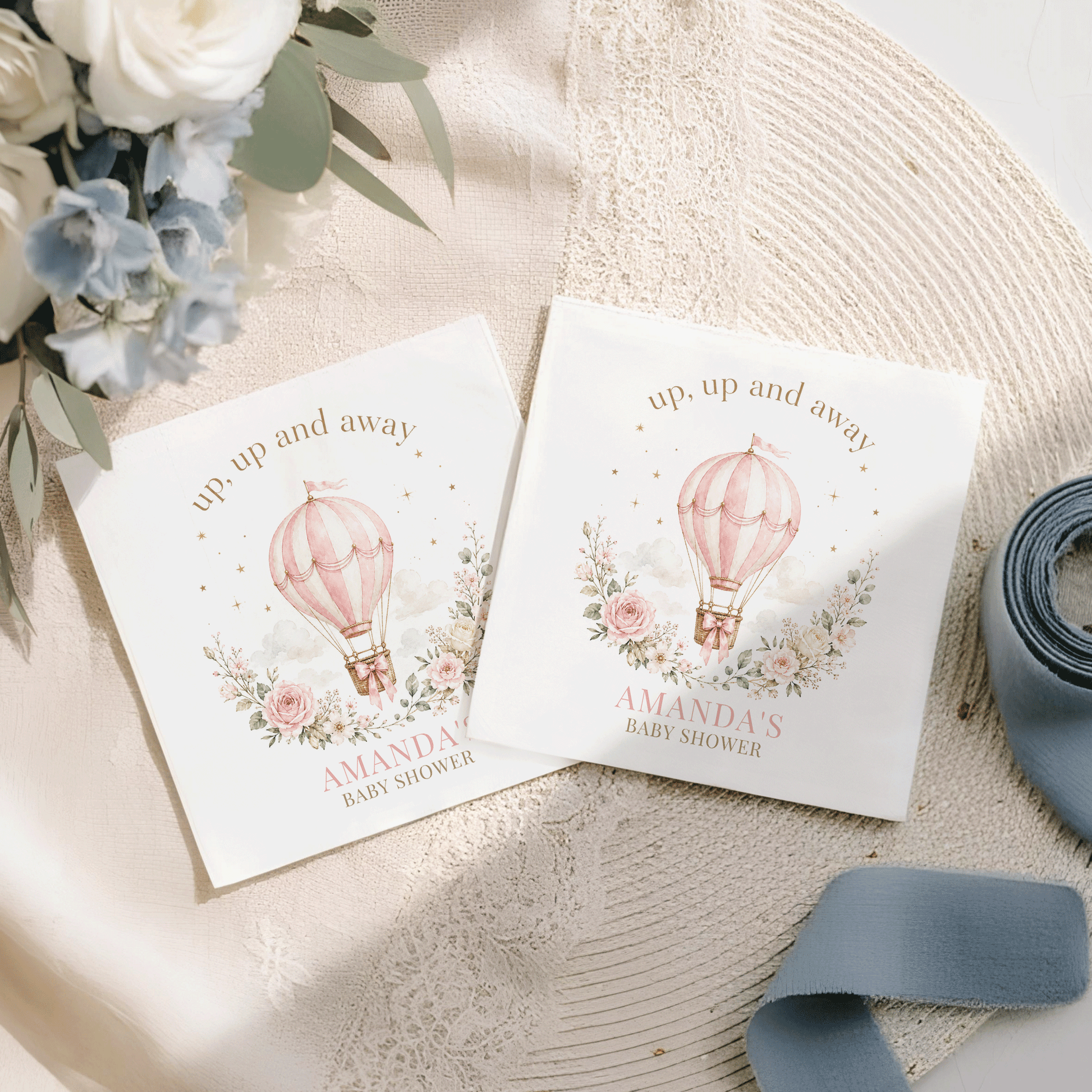 Two white napkins with a pink hot air balloon and flowers for Amanda's baby shower.