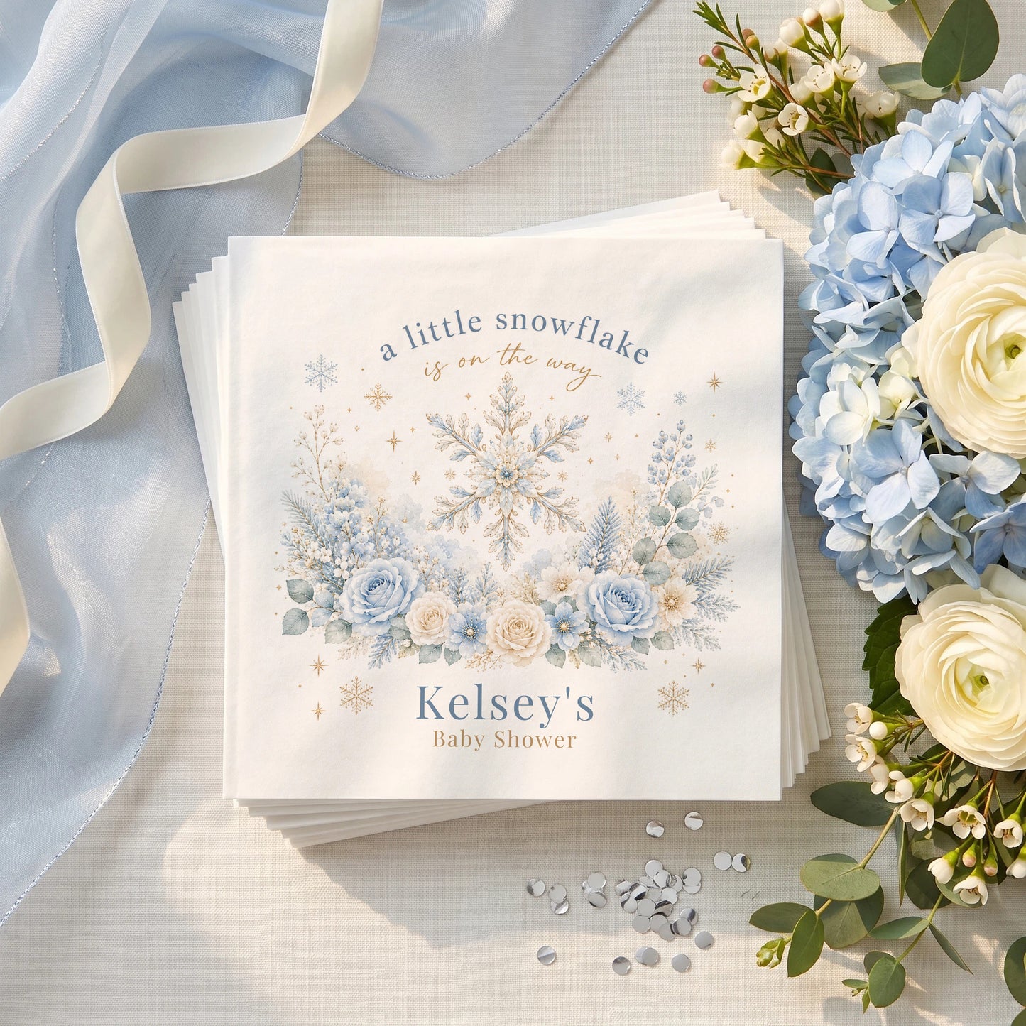 Icy blue baby shower napkin with a gold traced snowflake, blue roses, frosted pine and a personalized name in muted blue