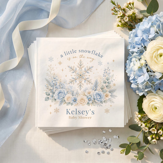 Icy blue baby shower napkin with a gold traced snowflake, blue roses, frosted pine and a personalized name in muted blue